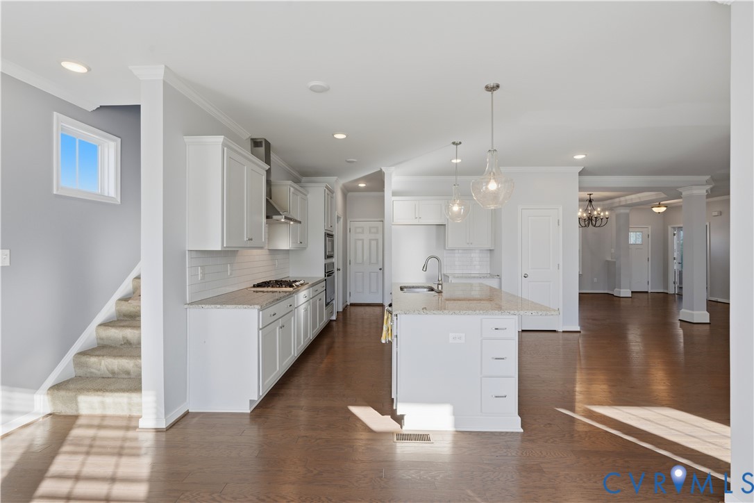 Kitchen featuring white shaker-style cabinetry, stone-surface countertops, a center island with undermount sink, pendant lighting, and wood-finish flooring
