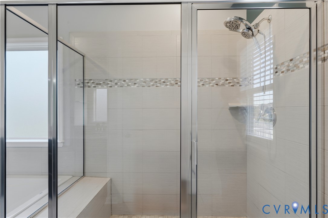 Downstairs Primary bathroom. Walk-in shower featuring a chrome-framed glass enclosure, floor-to-ceiling tile, decorative mosaic tile accent border, built-in corner shelving, and a multi-setting showerhead