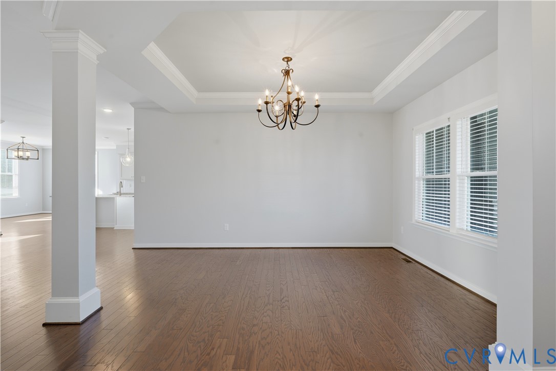 Open floor plan featuring wood-finish flooring, tray ceiling, architectural columns, and a central multi-arm chandelier