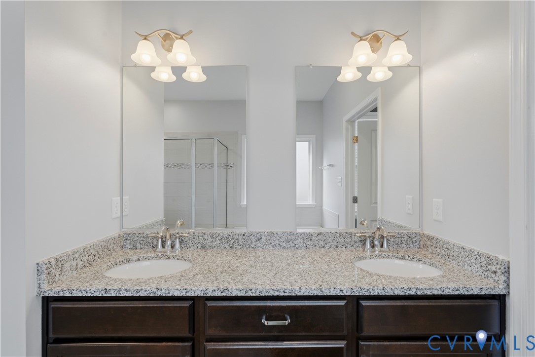 Downstairs Primary bathroom. Dual-sink vanity featuring stone-finish countertops, dark wood cabinetry, two separate plate-glass mirrors, and two three-light brushed-nickel fixtures with frosted glass shades