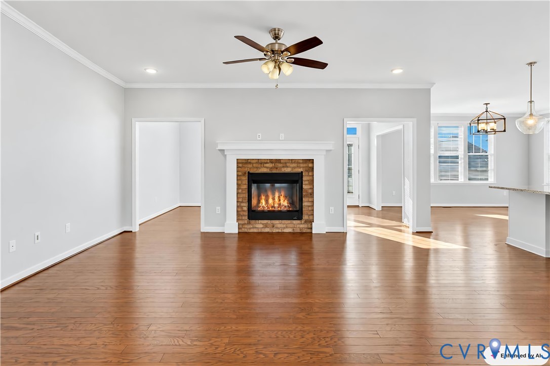Open-concept interior featuring wood-finish flooring, brick fireplace with a white mantel, crown molding, ceiling fan, and recessed lighting