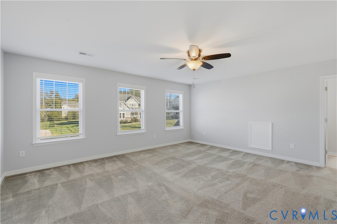 Upstairs Primary Bedroom or bedroom #2. Neutral-toned room featuring neutral wall-to-wall carpeting, three windows with horizontal blinds, and a central ceiling fan with integrated lighting