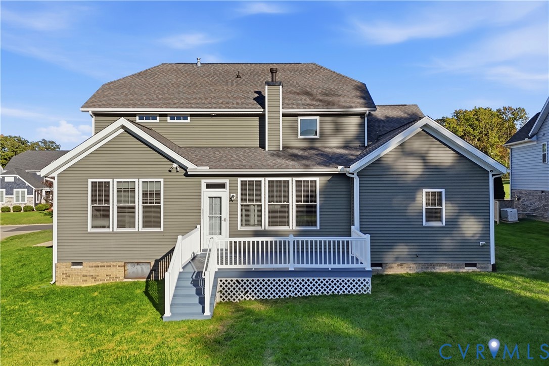 Two-story exterior featuring grey horizontal siding, a composite shingle roof, a raised deck with white railings, and a brick foundation trim