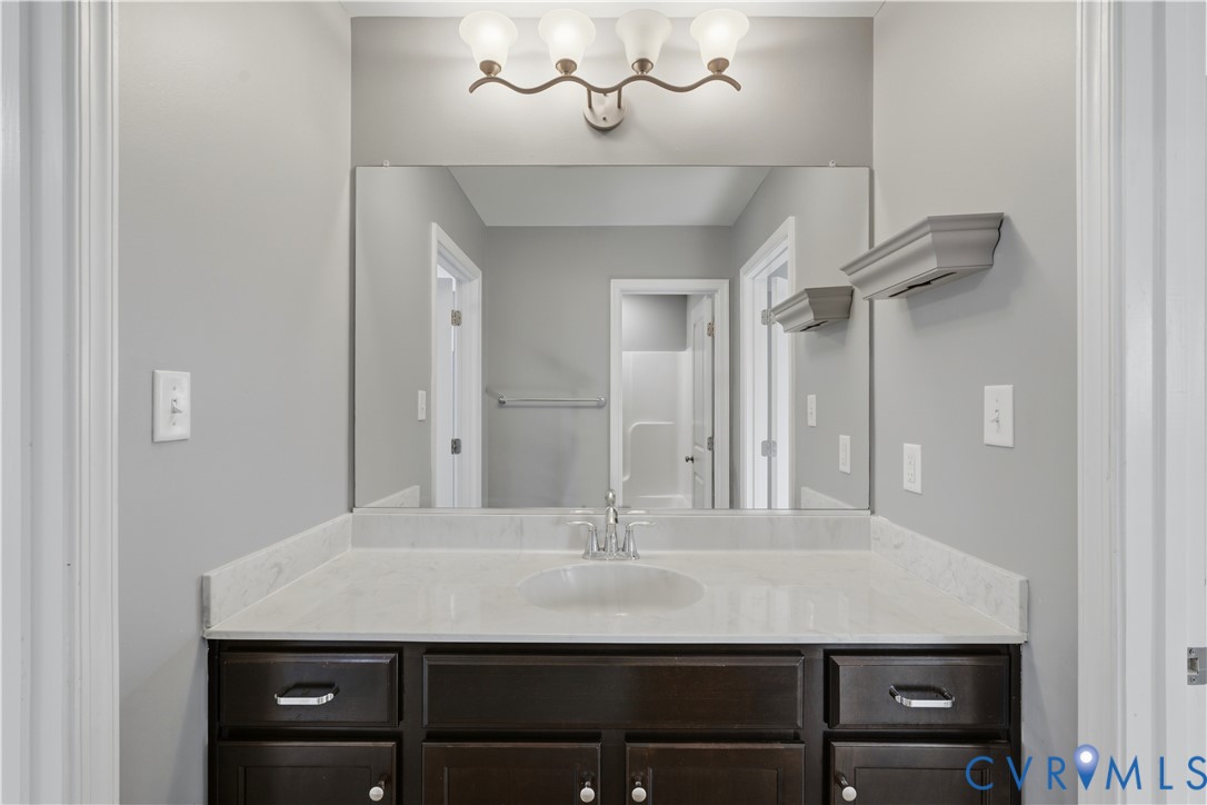 Jack and Jill upstairs bathroom. Dark-finish cabinetry with silver-tone hardware, stone-composite countertop with integrated sink, four-light vanity fixture, and large-format wall mirror