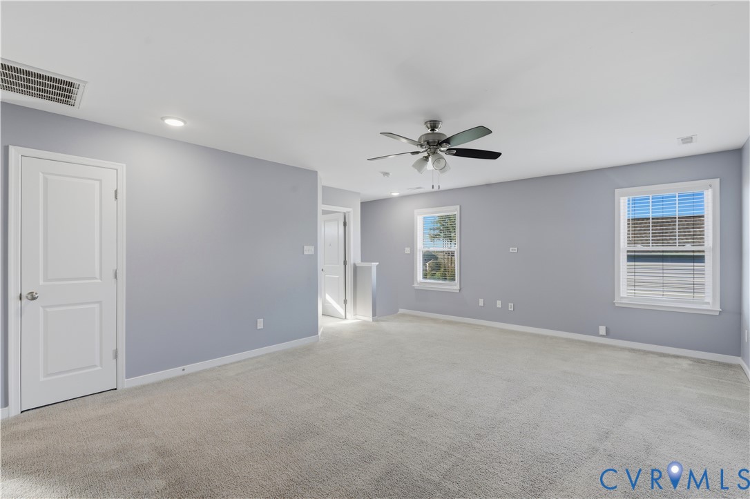 Neutral-toned interior space featuring neutral wall-to-wall carpeting, recessed ceiling lighting, a multi-blade ceiling fan with integrated light fixture, and windows with white casings