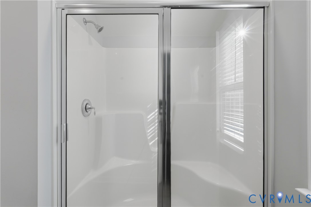 Upstairs Primary Walk-in shower enclosure featuring a white seamless surround, integrated seating, polished chrome hardware, and a semi-frameless glass door