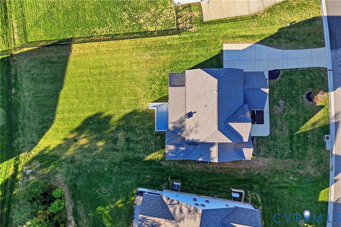 Aerial perspective of a multi-level residence featuring a multi-gabled shingle roof, a concrete driveway, and a spacious side lawn