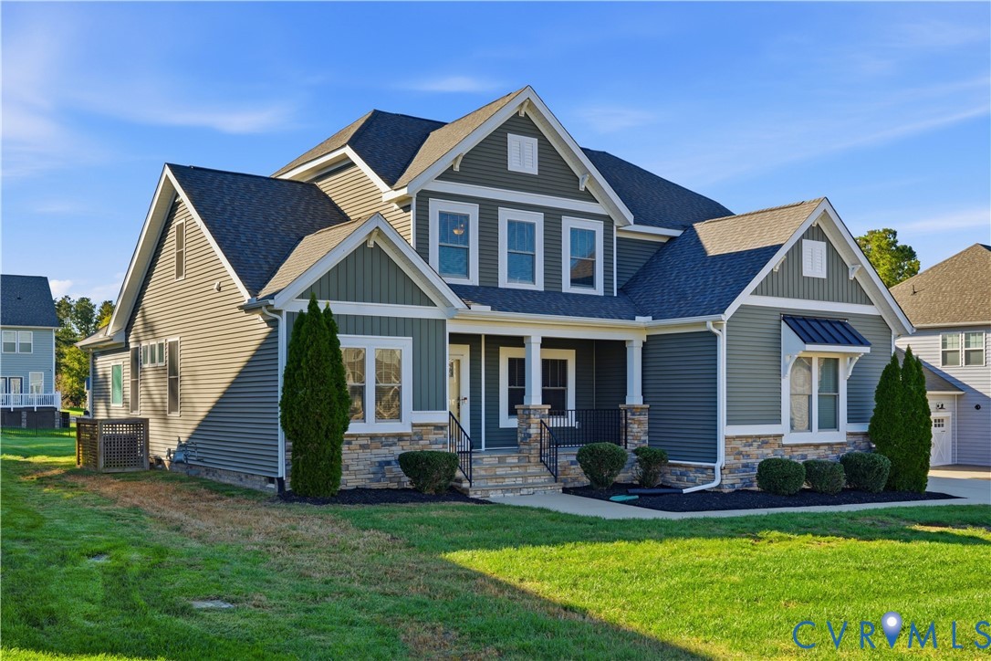 Two-story exterior featuring dark lap siding, stone veneer foundation, metal shed roof accent, a covered front porch with square columns, and multi-gabled roofline