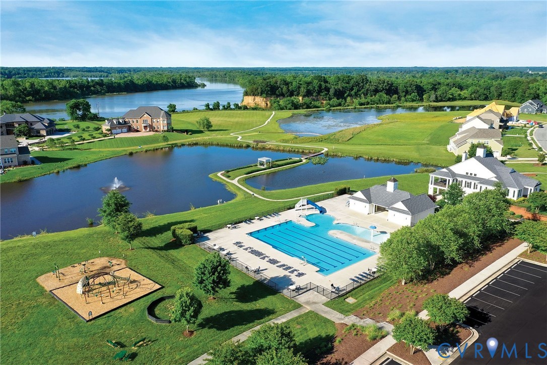 Community swimming pool with lap lanes and a slide, dedicated playground area, expansive landscaped grounds, central water feature with fountain, paved parking and clubhouse.