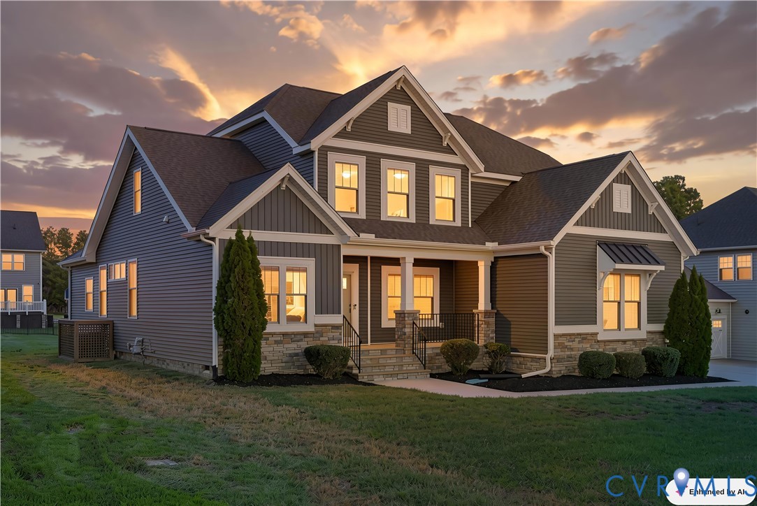 Two-story traditional exterior featuring horizontal siding, stone veneer foundation, multi-gabled roofline, covered front porch with stone-clad columns, and a metal-roofed accent awning