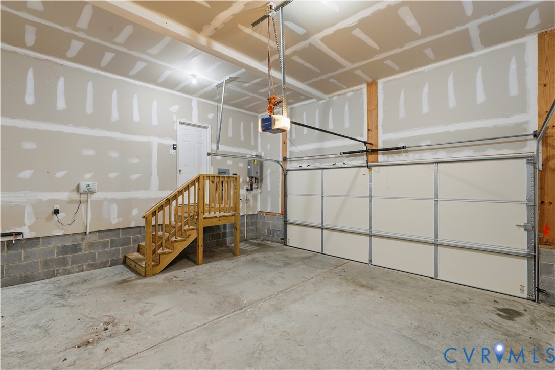 Two-car garage featuring a sectional overhead door, concrete flooring, exposed masonry block walls, and a built-in wooden staircase