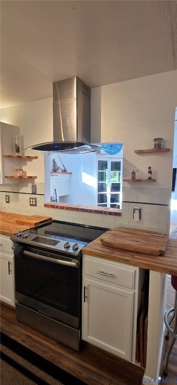 Kitchen featuring stainless steel range, professional-style stainless steel chimney hood, wood-finish countertops, subway tile backsplash, and built-in floating shelves Kitchen featuring stainless steel range, professional-style stainless steel chimney hood, wood-finish countertops, subway tile backsplash, and built-in floating shelves