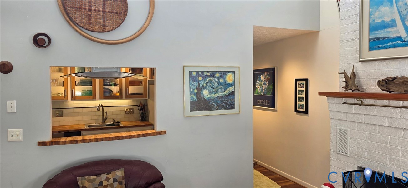 Interior space featuring a vaulted ceiling, painted brick fireplace with a wood mantel, and a pass-through window with a wood-finish counter Interior space featuring a vaulted ceiling, painted brick fireplace with a wood mantel, and a pass-through window with a wood-finish counter