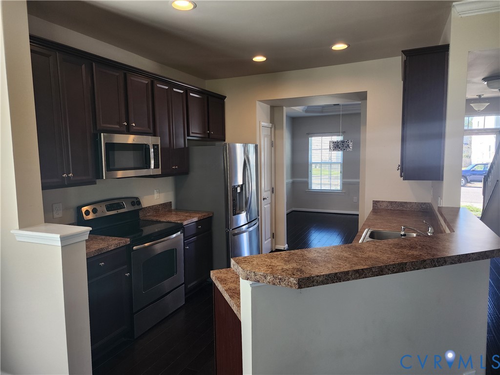 Kitchen featuring dark cabinetry, stainless steel appliances, speckled laminate countertops, recessed lighting, and wood-finish flooring