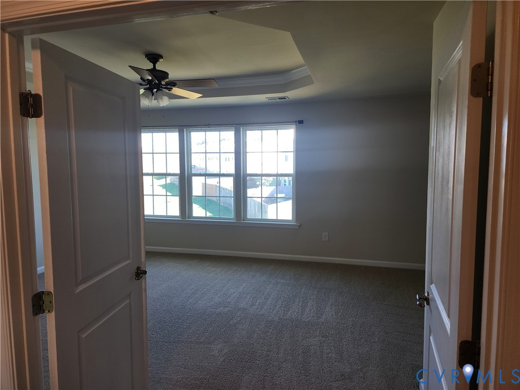 Double-door entry featuring neutral wall-to-wall carpeting, tray ceiling, integrated ceiling fan with light kit, and a triple-pane grid window configuration