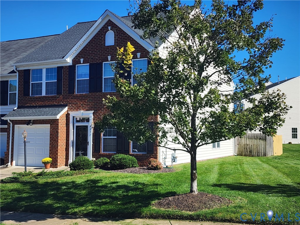 Two-story brick and siding exterior featuring dark shutters, a gabled roofline, an attached one-car garage, and a manicured lawn