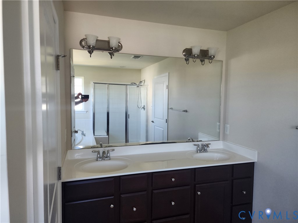 Double vanity with a solid-surface countertop, dual integrated sinks, dark wood-finish cabinetry, a full-width vanity mirror, and dual wall-mounted light fixtures