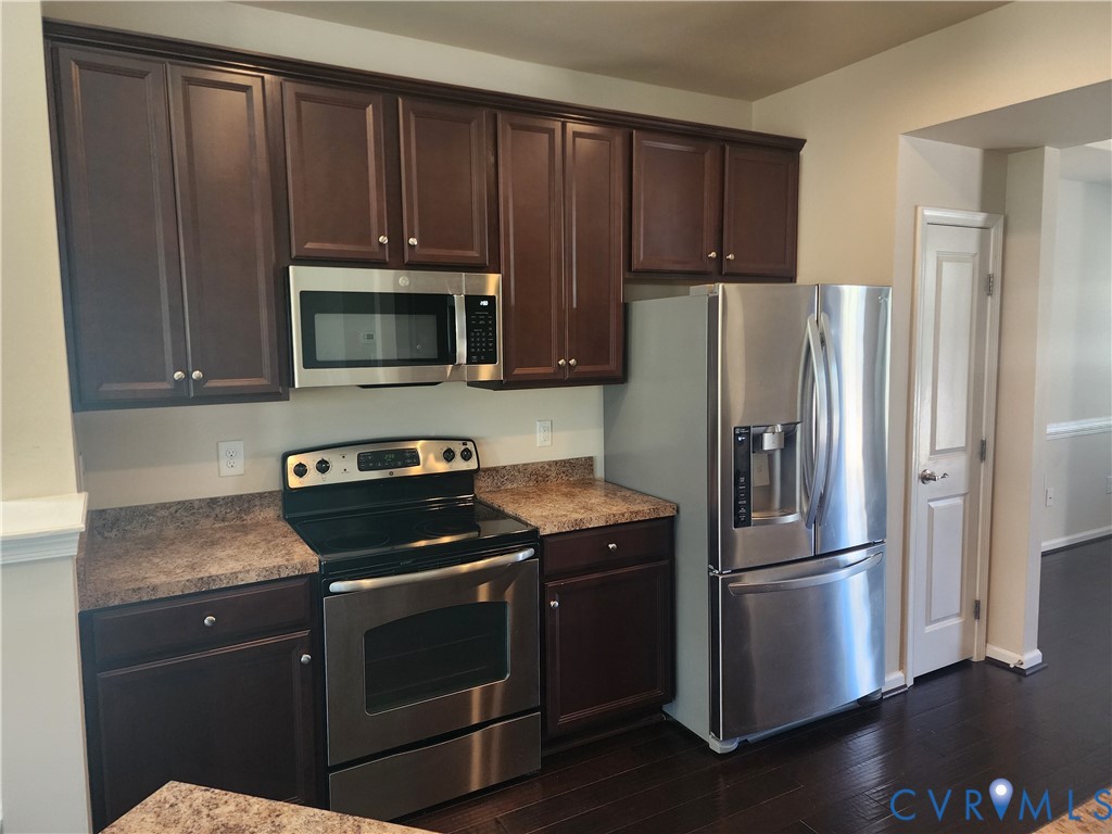 Dark wood-finish cabinetry, stainless steel appliances, speckled laminate countertops, and dark wood-finish flooring