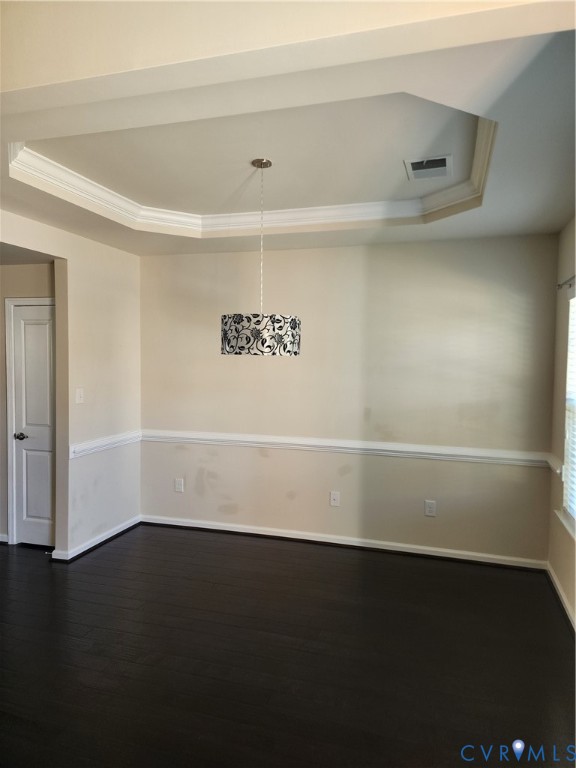 Tray ceiling with crown molding, dark wood-finish flooring, chair rail wainscoting, and drum pendant lighting