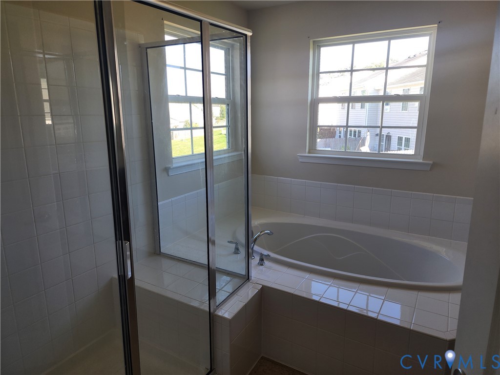 Bathroom featuring a glass-enclosed shower, built-in soaking tub with tiled surround, and dual pane windows