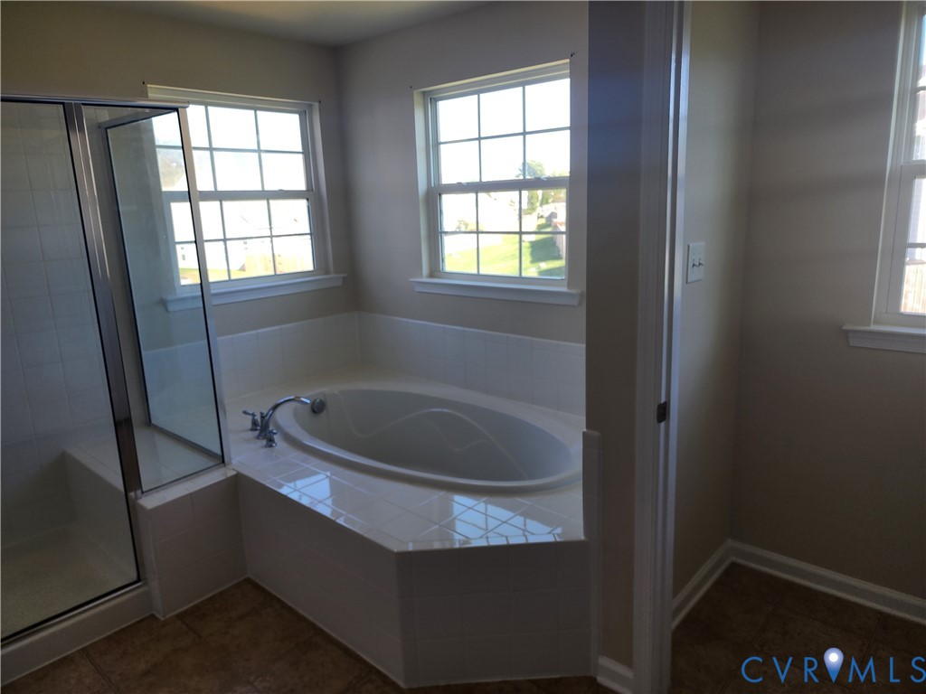 Oval soaking tub with a tiled surround, separate glass-enclosed shower, grid-pattern windows, and tile flooring