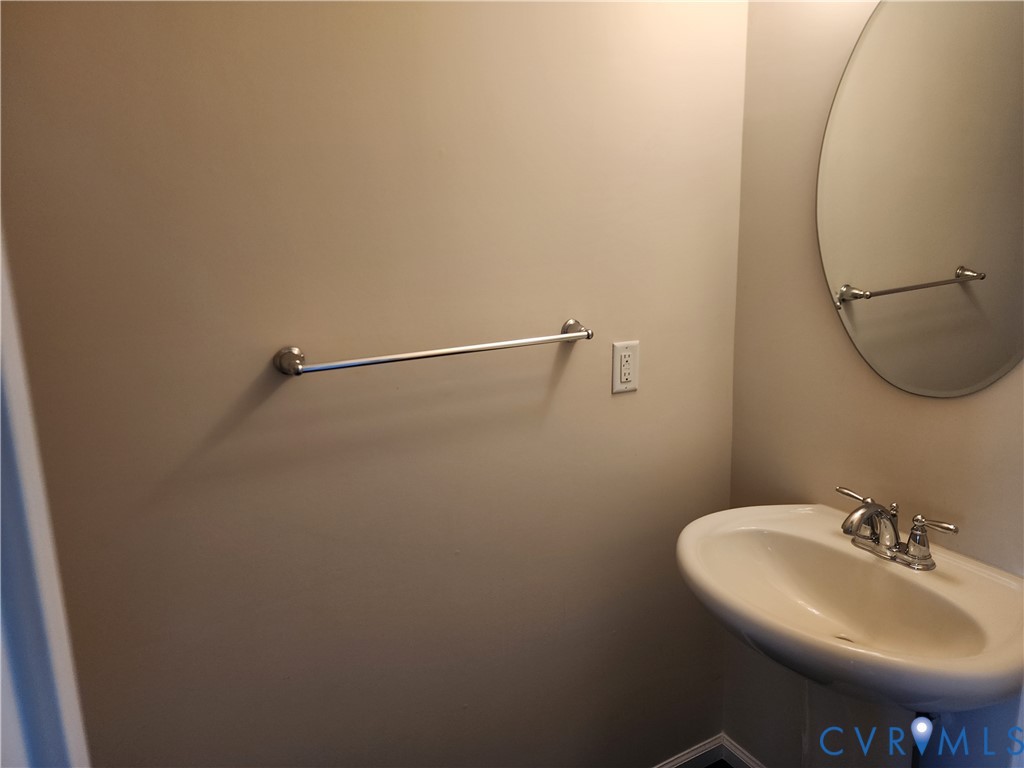 Pedestal sink with a two-handle chrome faucet, oval wall-mounted mirror, and brushed nickel towel bar