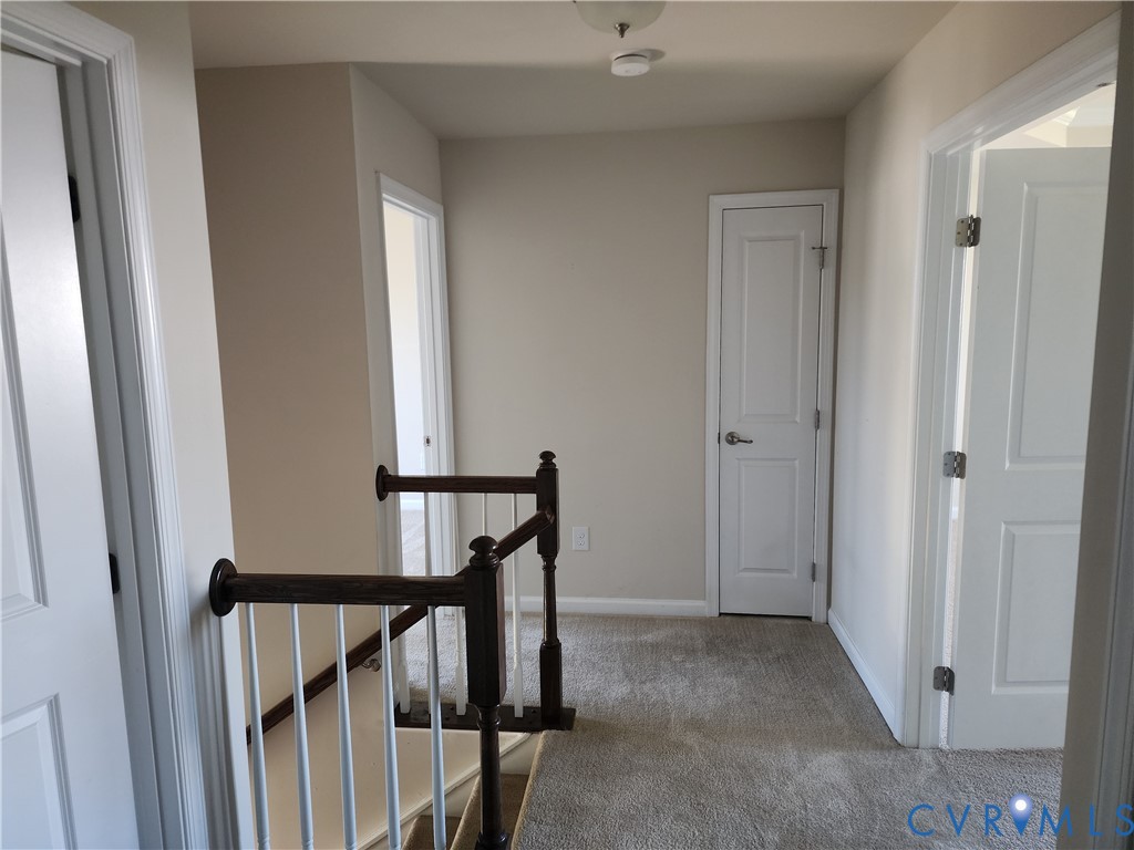Hallway featuring neutral wall tones, wall-to-wall carpeting, white two-panel interior doors, and a wood-finish handrail with white balusters