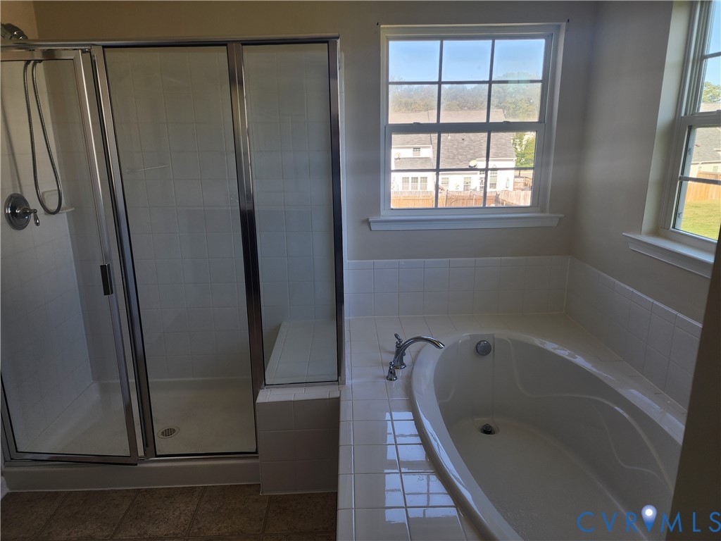 Oversized soaking tub with white tile surround, separate glass-enclosed shower, and dual multi-pane windows