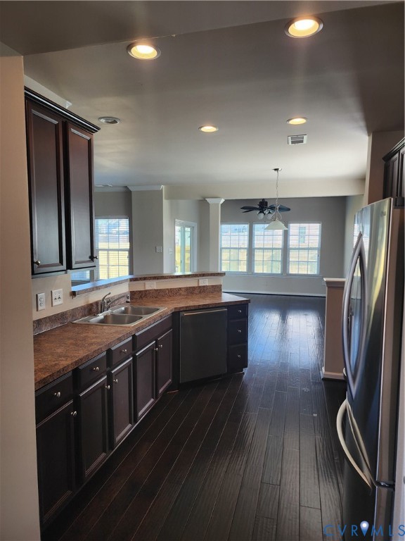 Kitchen featuring dark wood-finish cabinetry, stainless steel appliances, dual-basin sink, and recessed lighting, with wood-finish flooring extending throughout the area