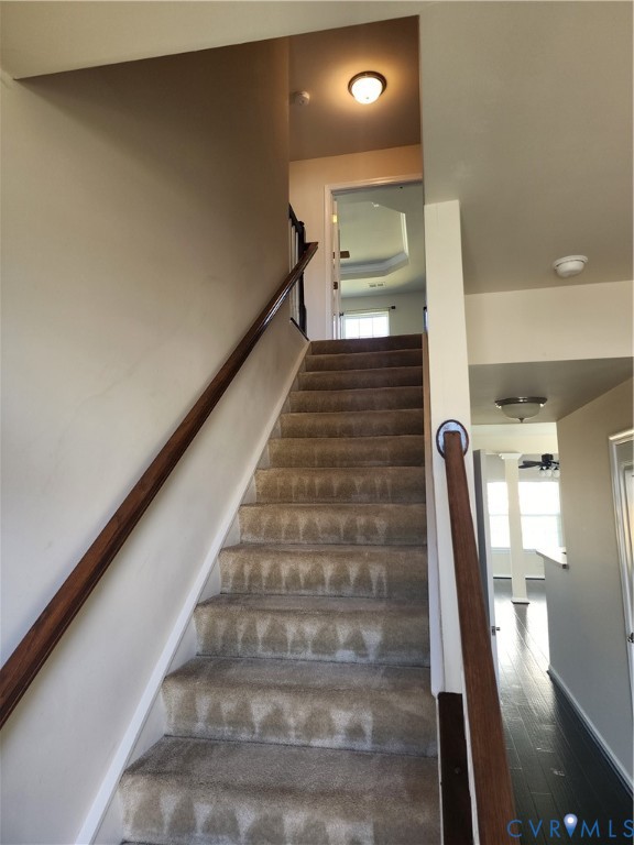 Staircase featuring neutral carpeted treads, wood-finish handrails, and flush-mount lighting fixtures