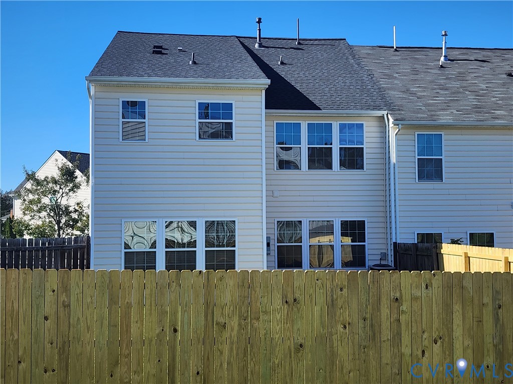 Two-story light-colored siding exterior with a shingled roof, multi-pane windows, and a privacy wood fence