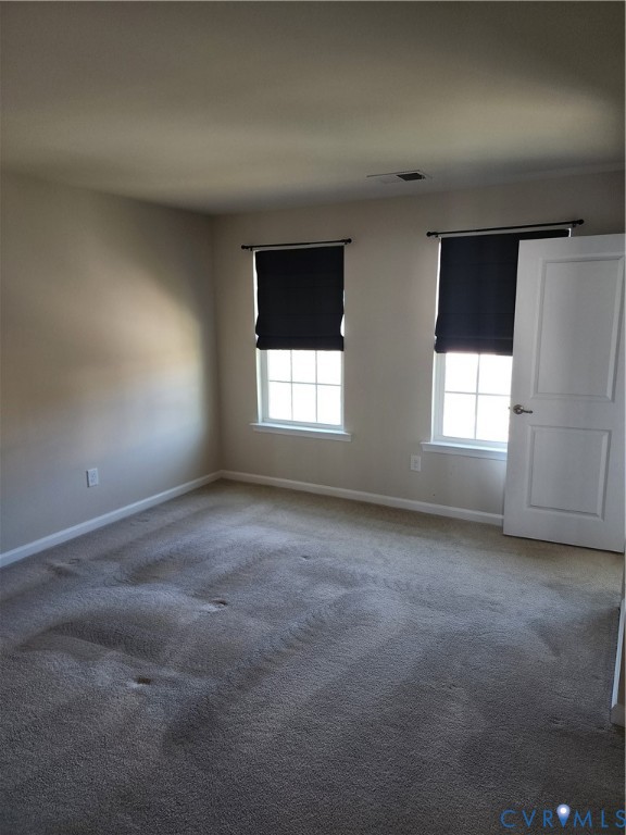 Neutral-toned interior room featuring wall-to-wall carpeting, two windows with muntin dividers, and a six-panel door with a brushed nickel lever