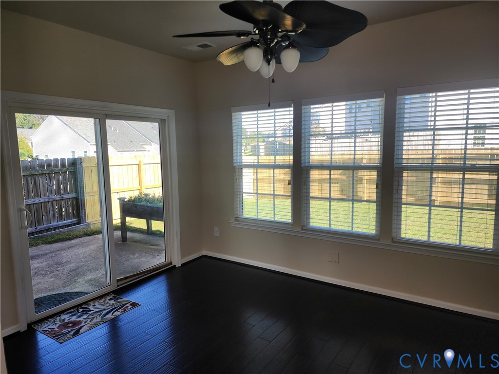 Dark-toned wood-finish flooring, sliding glass door, three windows with horizontal blinds, and a multi-blade ceiling fan with integrated lighting