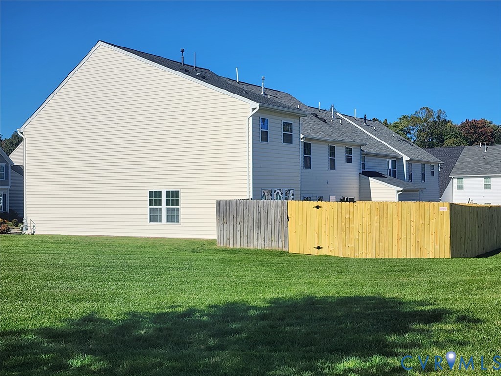 Exterior featuring light-colored horizontal siding, asphalt shingle roof, double-hung windows, and a fenced backyard with a grass lawn