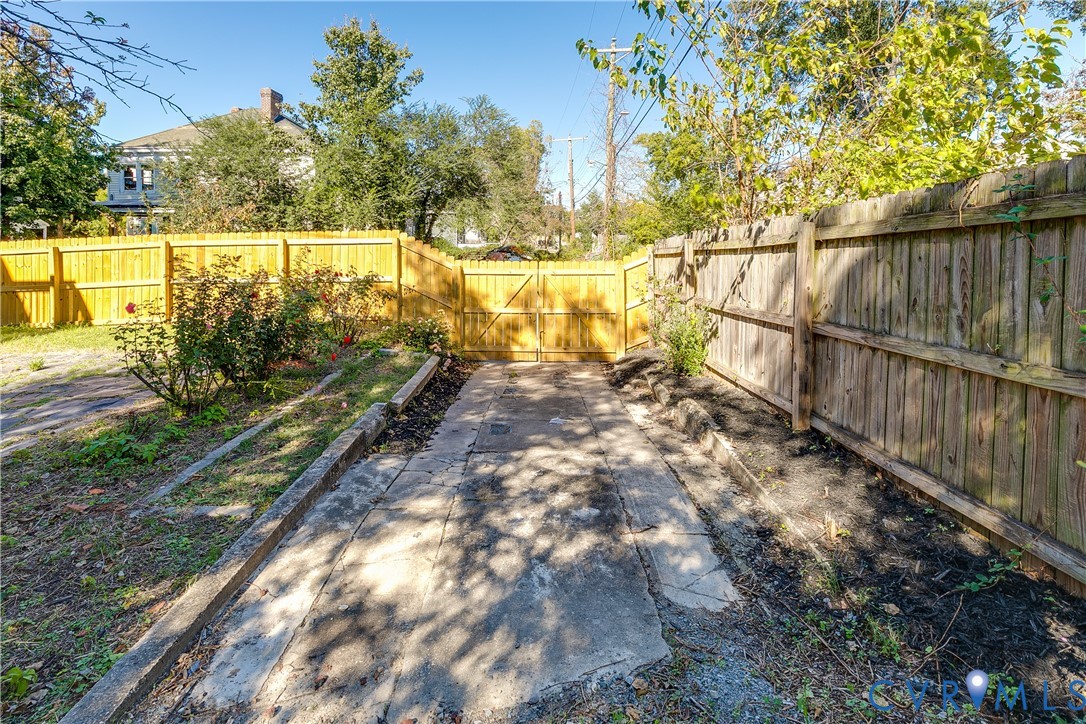 Fenced outdoor area featuring a concrete surface, wood-style gate, and mature landscaping