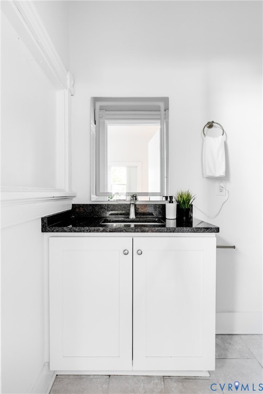 White cabinetry vanity with a dark stone countertop, integrated undermount sink, chrome faucet, and rectangular wall-mounted mirror