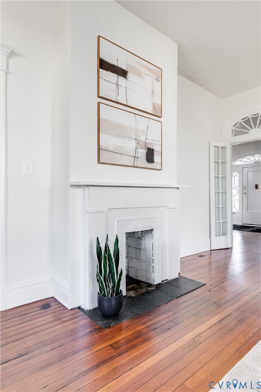 Fireplace featuring a classic mantelpiece and a dark stone hearth, complemented by wood-finish flooring, high ceilings, and an arched transom window