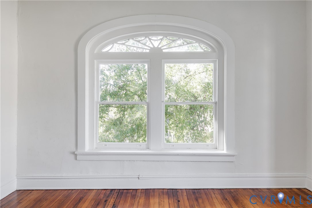 Arched window featuring a segmented fanlight, double-hung sash, and detailed trim, set against neutral wall finishes and wood-finish flooring