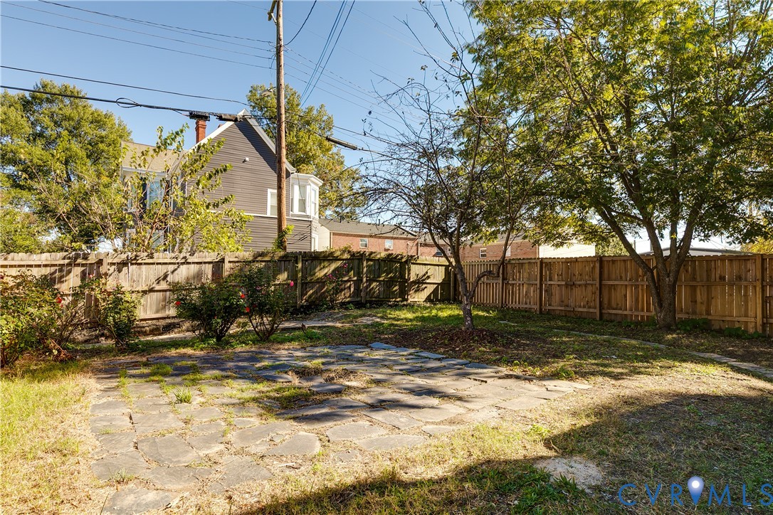 Backyard featuring a stone-paver patio, wood-slat perimeter fencing, and mature trees