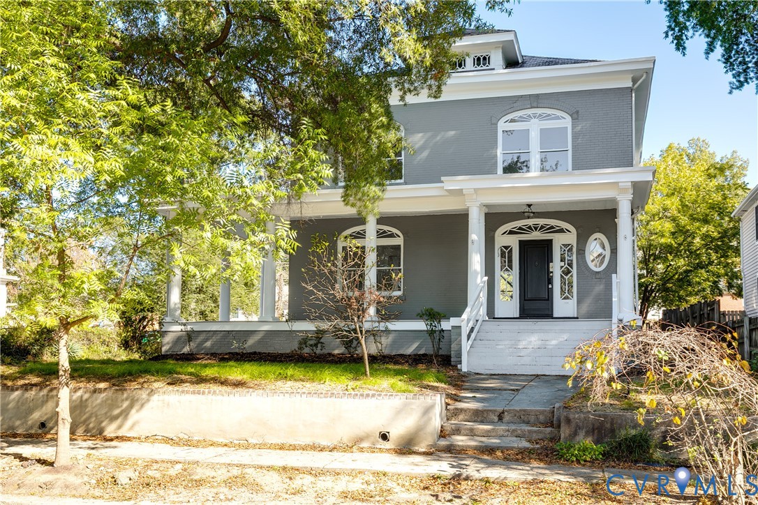 Two-story exterior featuring painted masonry siding, a wrap-around porch with classical columns, arched window detailing, and a front entrance with an arched transom and sidelights