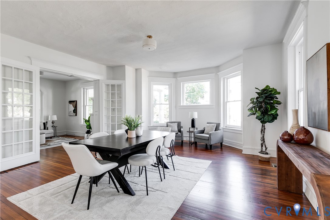 Dining area featuring wood-finish flooring, a three-panel bay window, and double French doors with glass panes