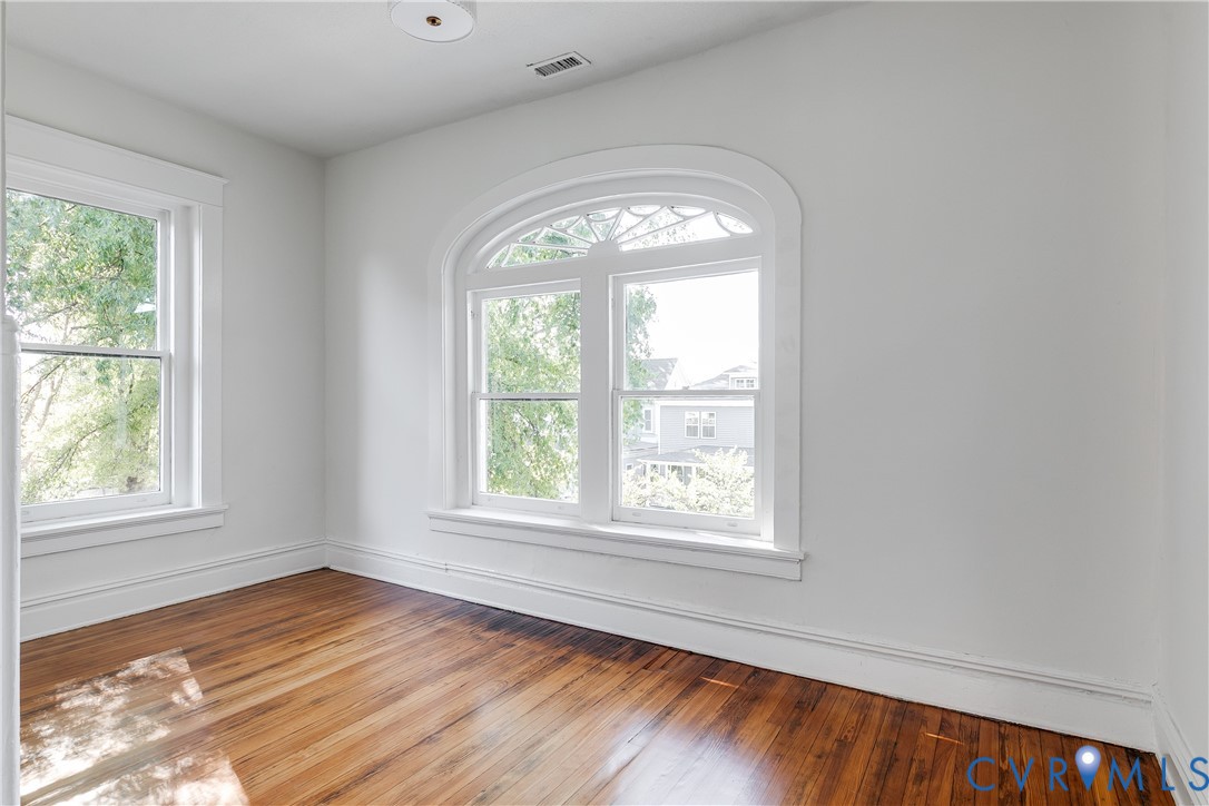 Room featuring wood-finish flooring, a prominent arched window with decorative transom, and a secondary rectangular window with wide white trim