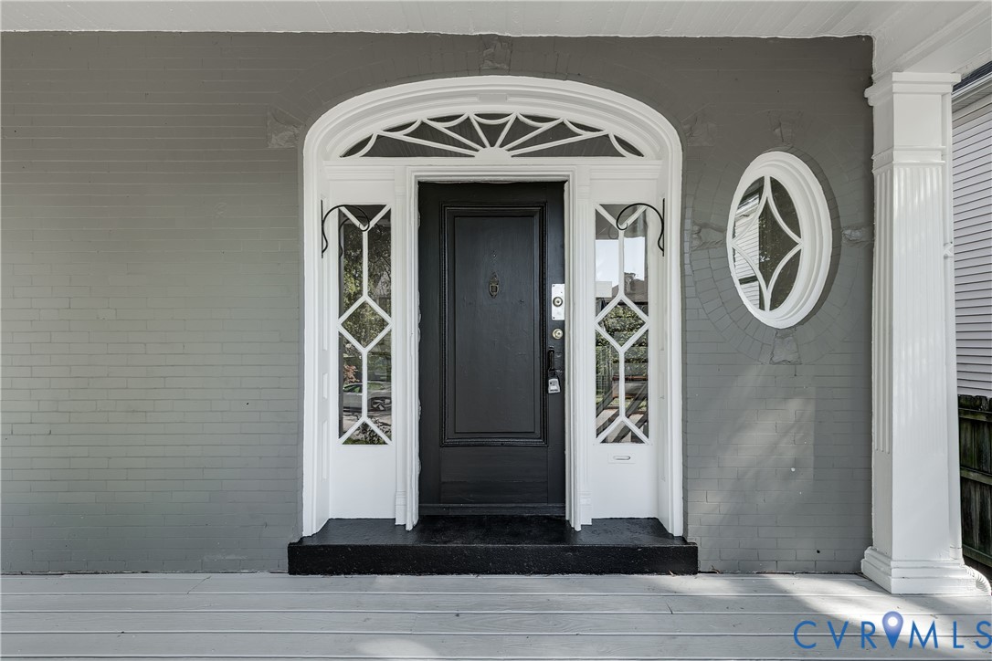 Painted brick exterior featuring a front entrance with a sunburst transom window, decorative sidelights, an oval accent window, and a fluted porch column