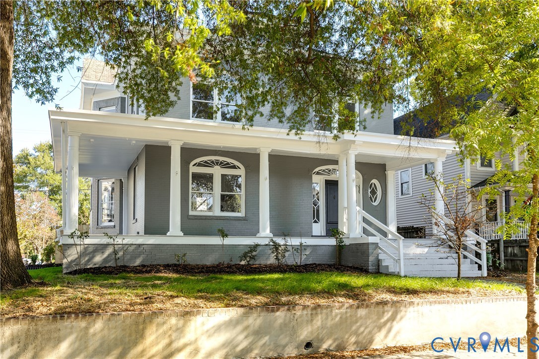 Two-story painted brick exterior featuring a wide covered front porch with classical columns, arched window detailing, and a multi-light transom door