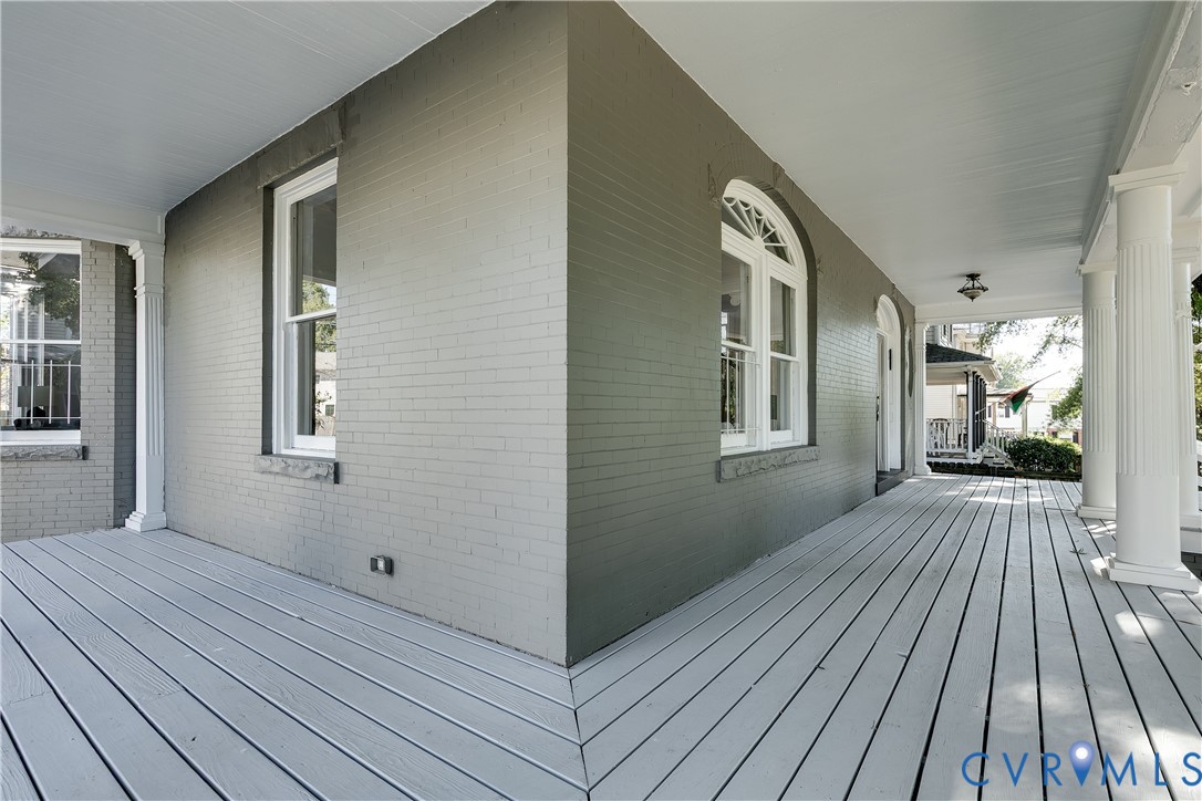 Covered porch featuring painted brick exterior, fluted columns, wood-plank decking, and arched window detailing