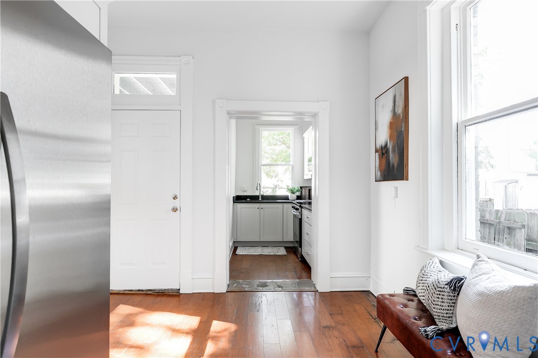 Wood-finish flooring, stainless steel refrigerator, white shaker-style cabinetry, and tall multi-pane windows