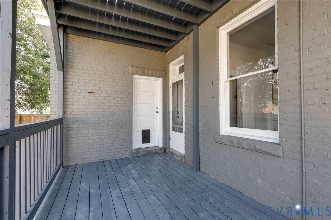 Covered porch featuring painted brick exterior walls, wood-plank flooring, and a fenced railing