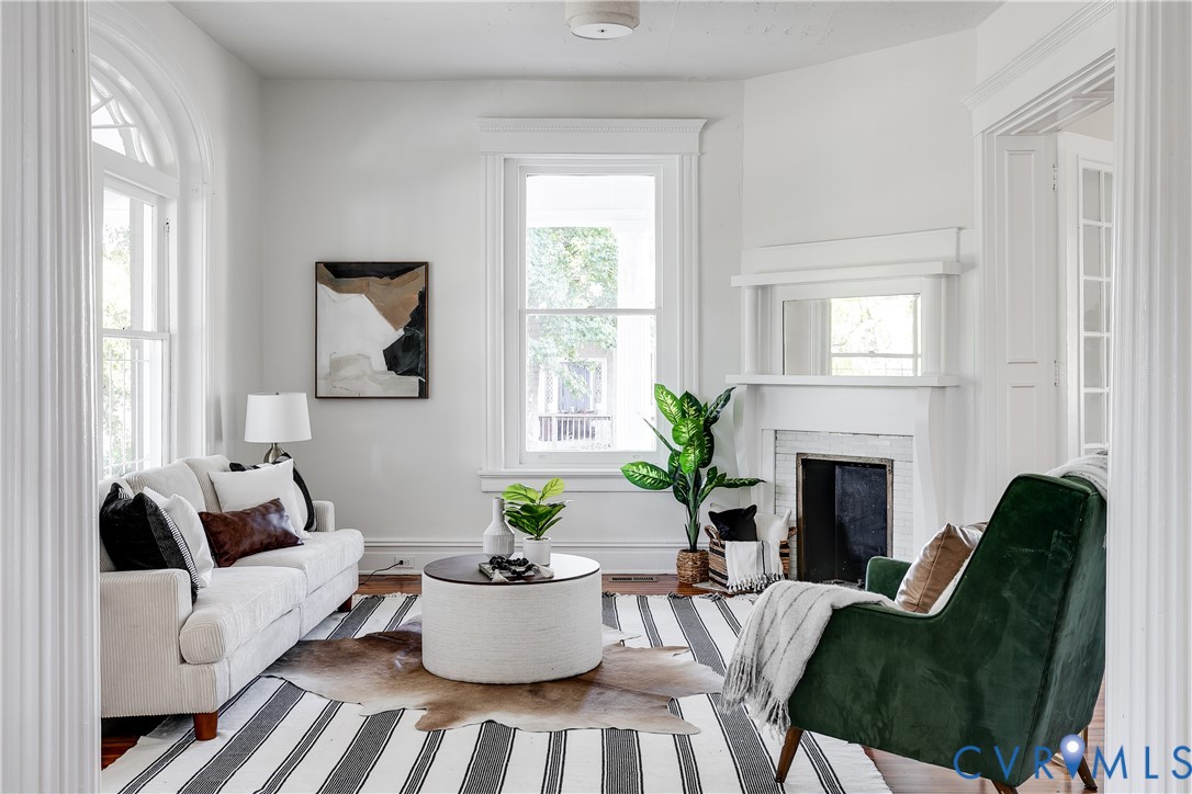 Architectural detailing featuring arched window trim, wood-finish flooring, a fireplace with a decorative mantel, and fluted column casing