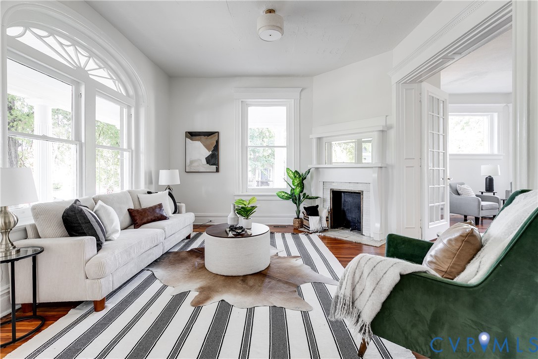 Living area featuring wood-finish flooring, a fireplace with an ornate mantel and mirror, large arched windows with transoms, and French doors