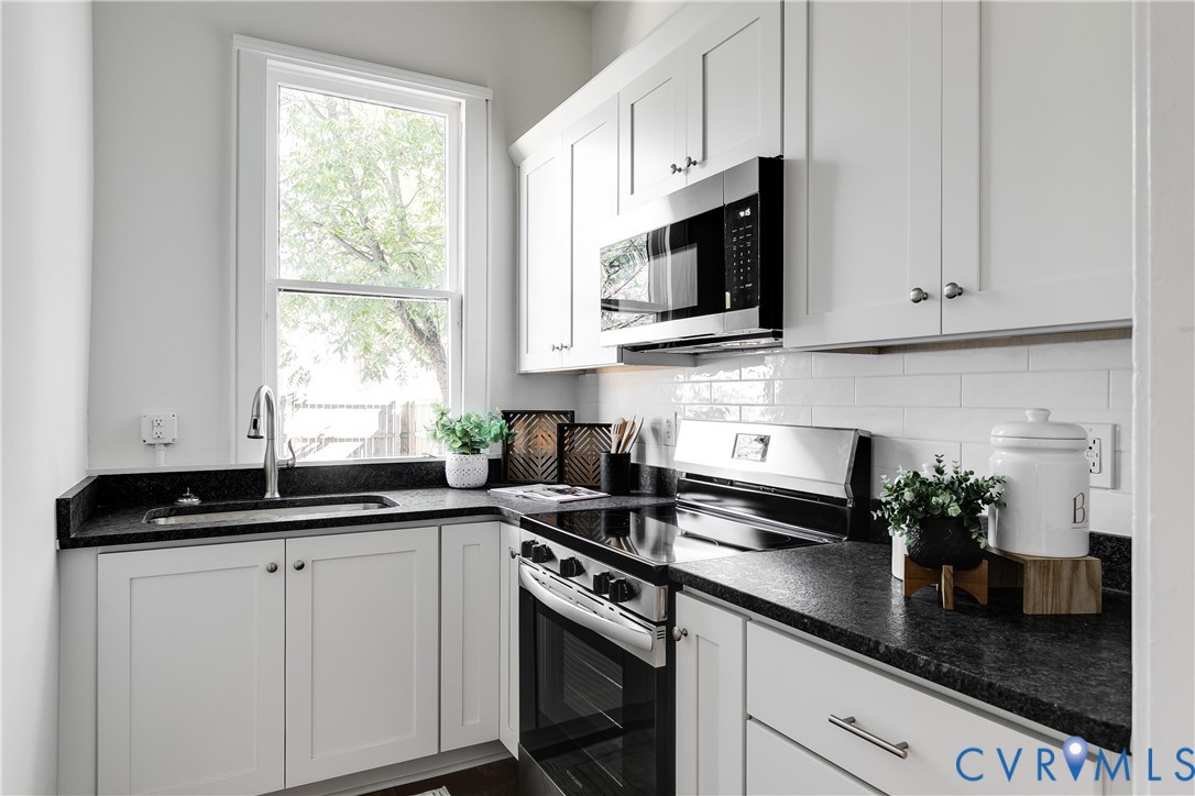 White shaker-style cabinetry, dark stone countertops, stainless steel appliance suite, and white subway tile backsplash